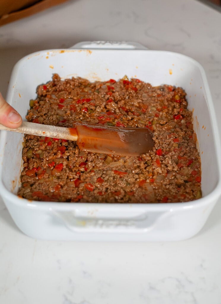 Meat mixture being spread into casserole dish.