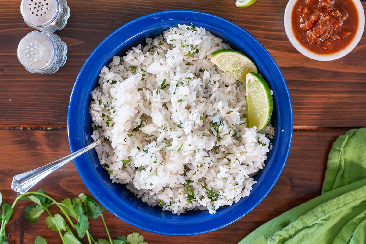 Cilantro lime rice in a blue bowl next to fresh cilantro.