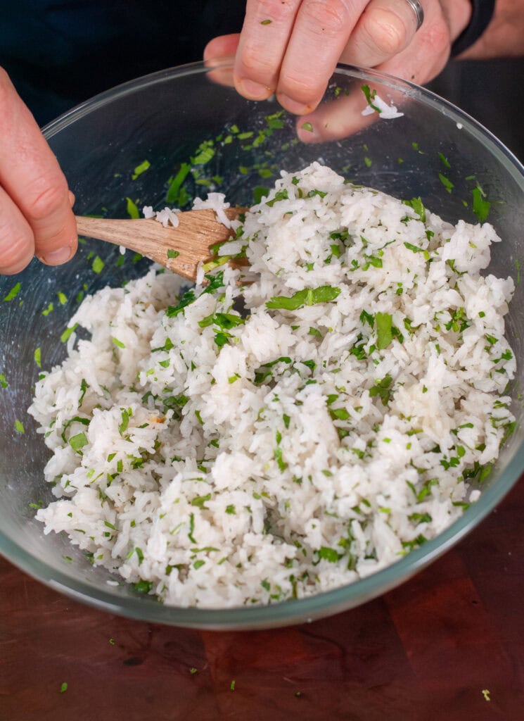 A wooden spoon mixing cilantro into rice.