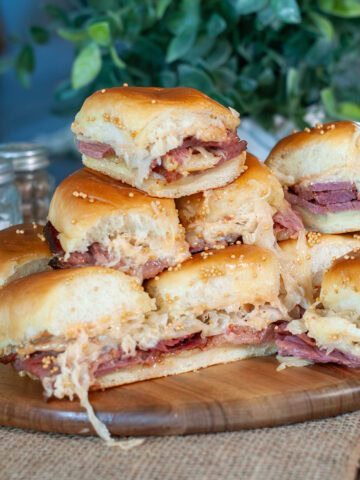 A pile of corned beef sliders on a wooden board.