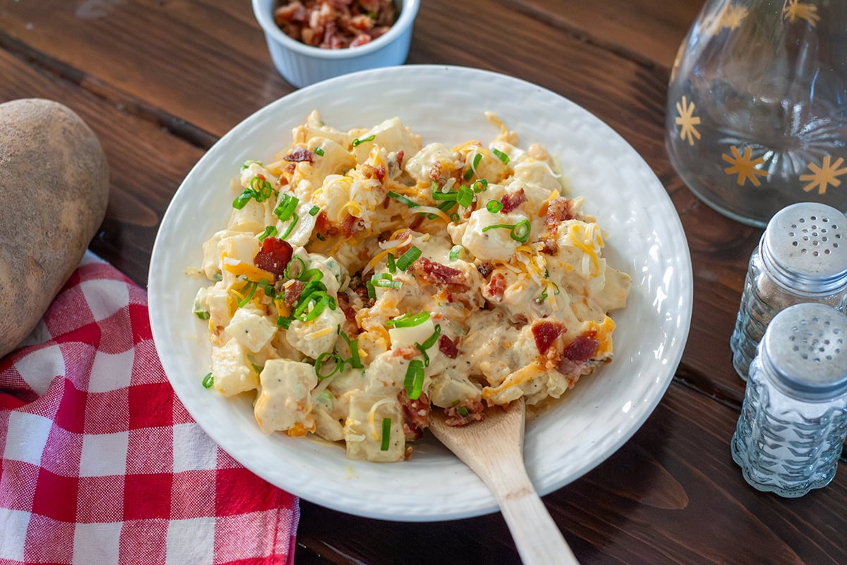 A bowl of loaded baked potato salad on a wooden table.