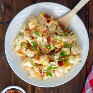 Loaded baked potato salad next to a bowl of bacon.