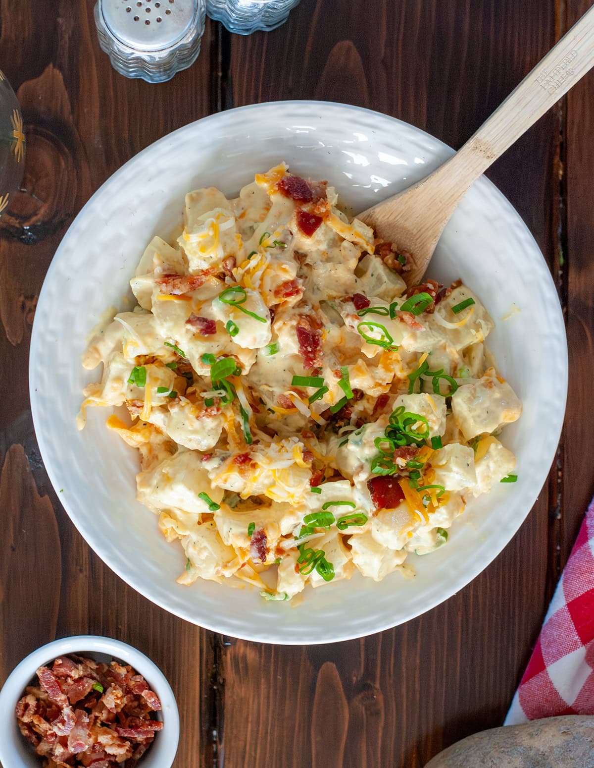 Loaded baked potato salad next to a bowl of bacon.