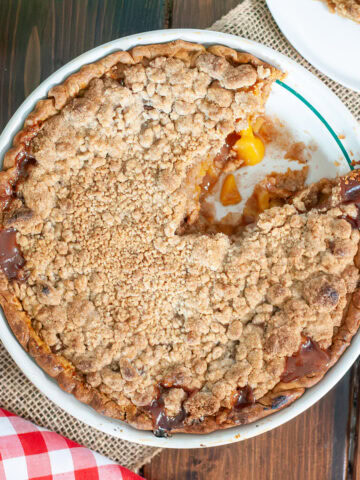 A peach mango pie with a crumble next to fruits.