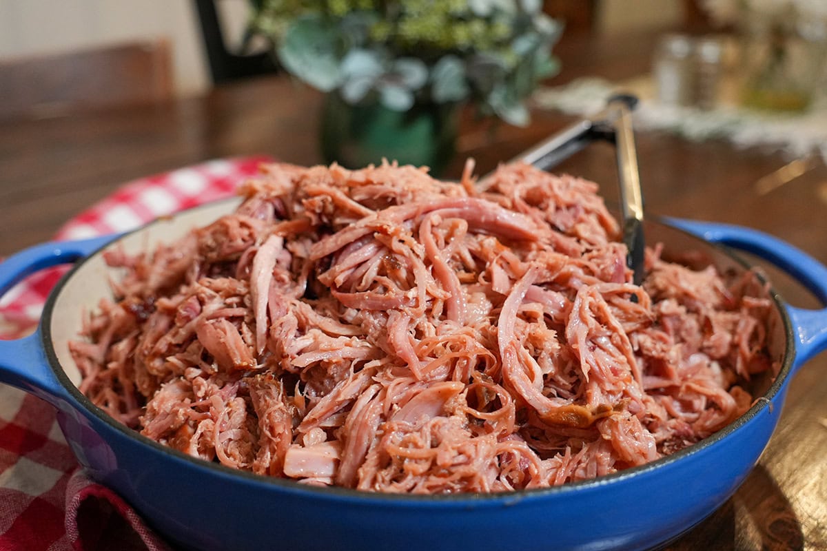 A bowl of pulled ham with tongs on a red cloth.