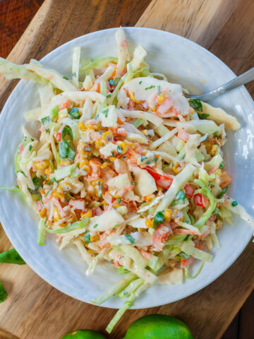 A bowl of corn claw next to limes and cilantro.
