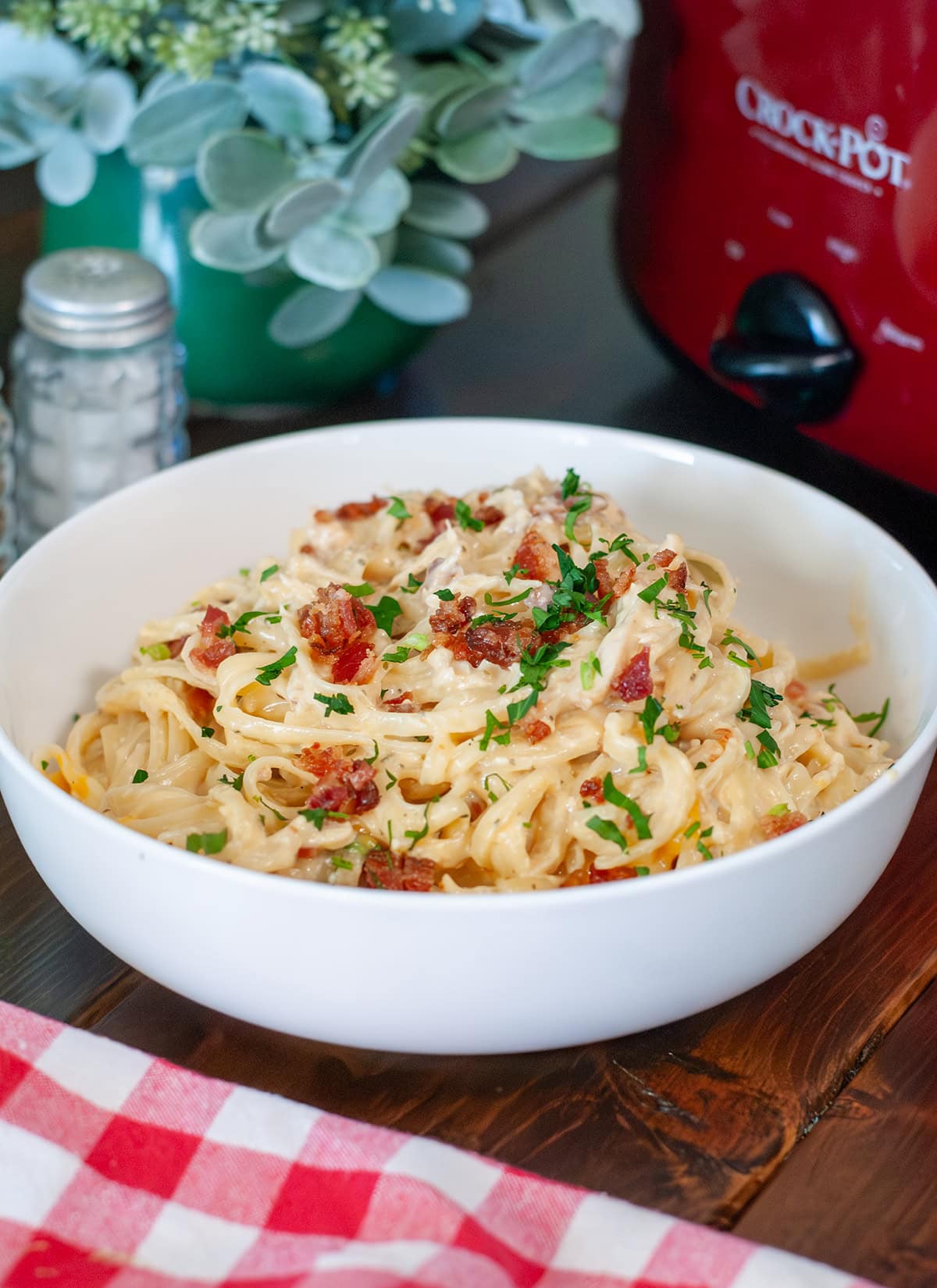 A bowl of chicken pasta next to a crock pot.