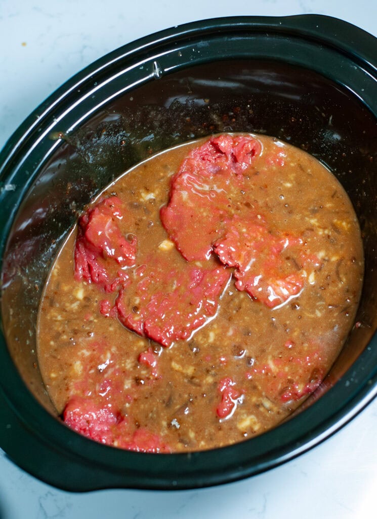 Cube steaks in a slow cooker with sauce ingredients.