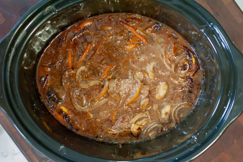 Cube steaks cooking in a crock pot with onions.