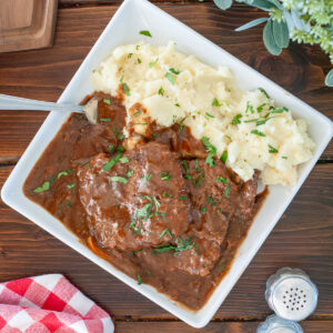 Cube Steak on a plate with mashed potatoes topped with parsley.