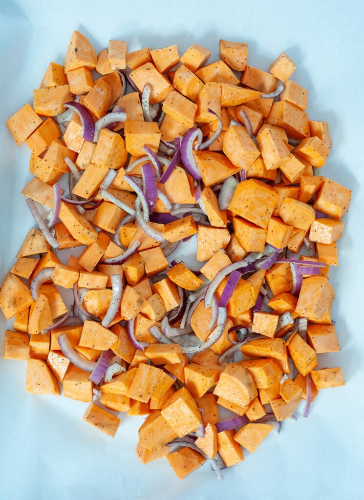 Seasoned sweet potatoes and onions on a baking sheet.