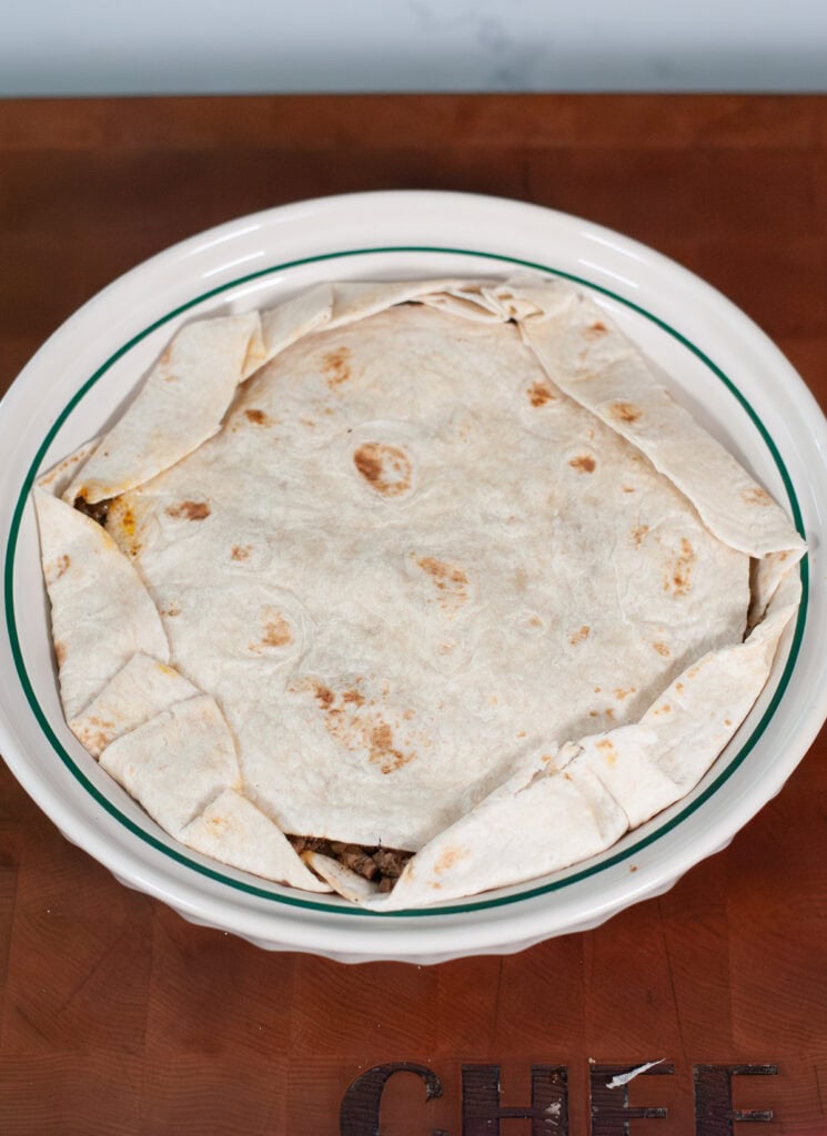A tortilla folded over meat in pie dish.