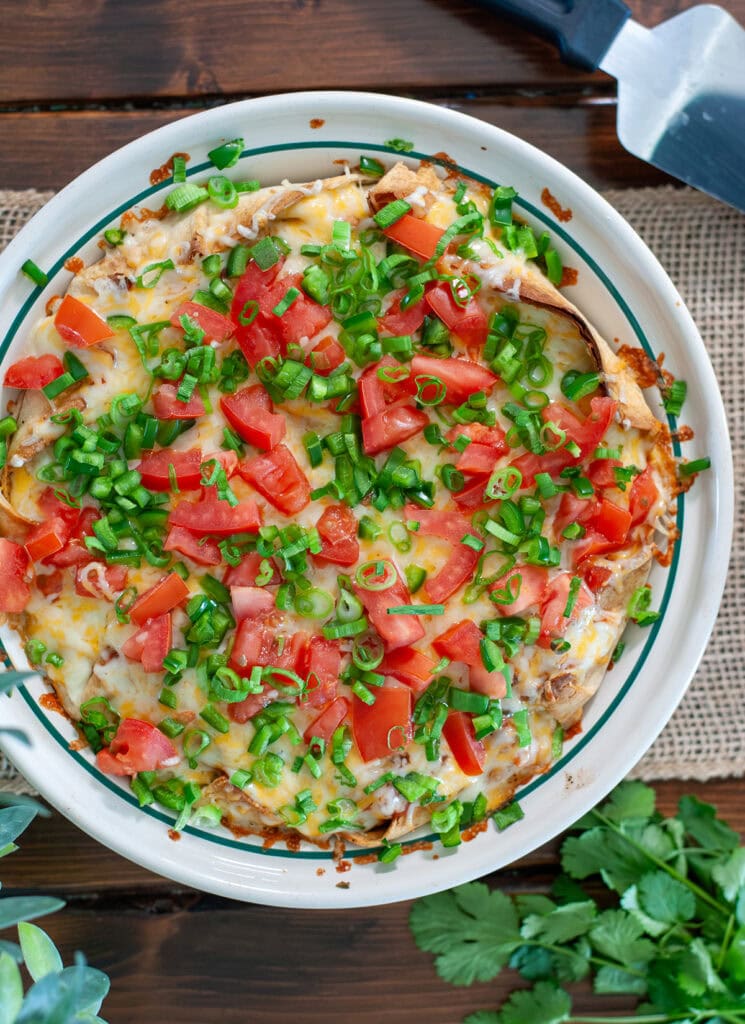 A baked taco pie with chives and tomatoes next to cilantro.