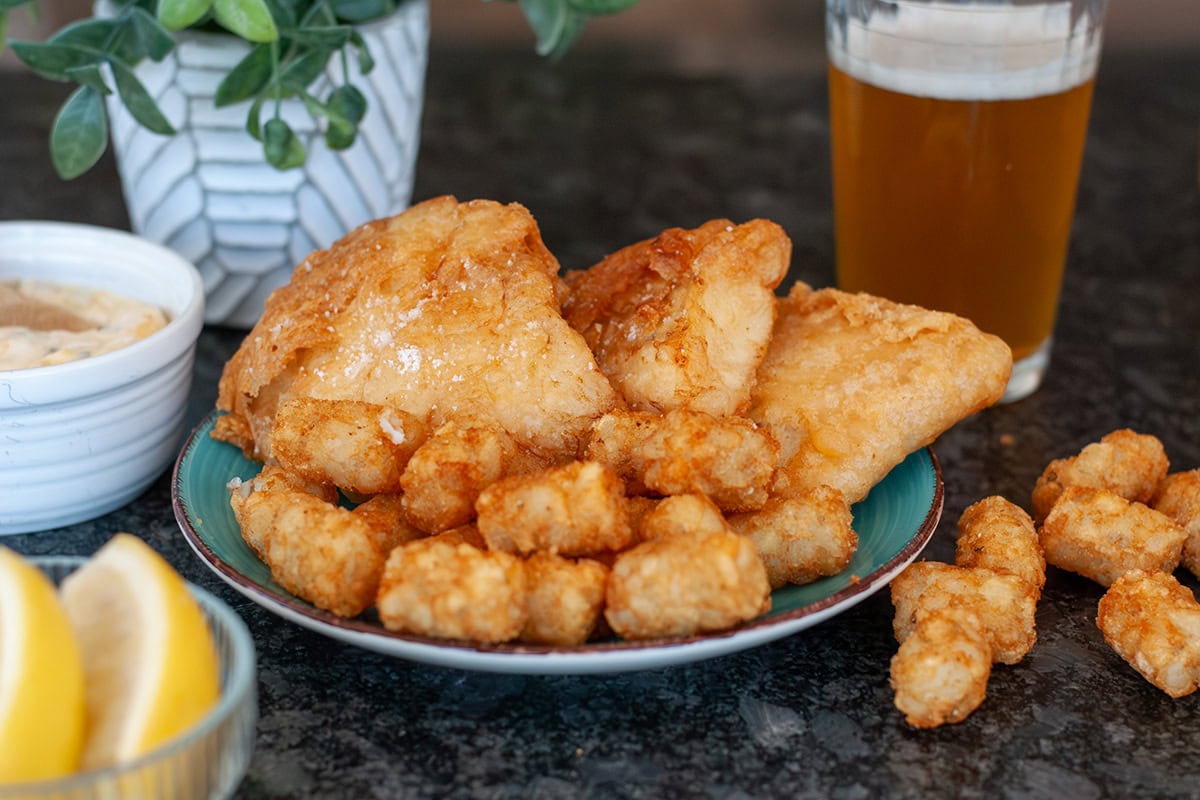 A plate of golden brown beer battered fish and tater tots.