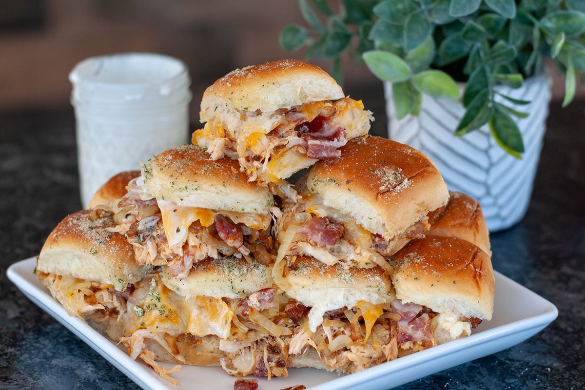 Chicken bacon ranch sliders piled up on a white plate.