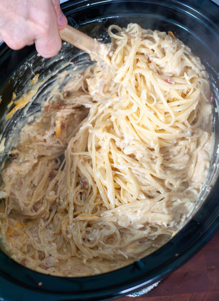 Noodles being mixed into crock pot with shredded chicken and sauce.