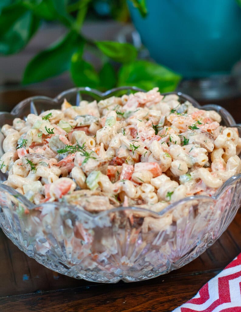 Combined macaroni salad ingredients in a glass bowl topped with dill.