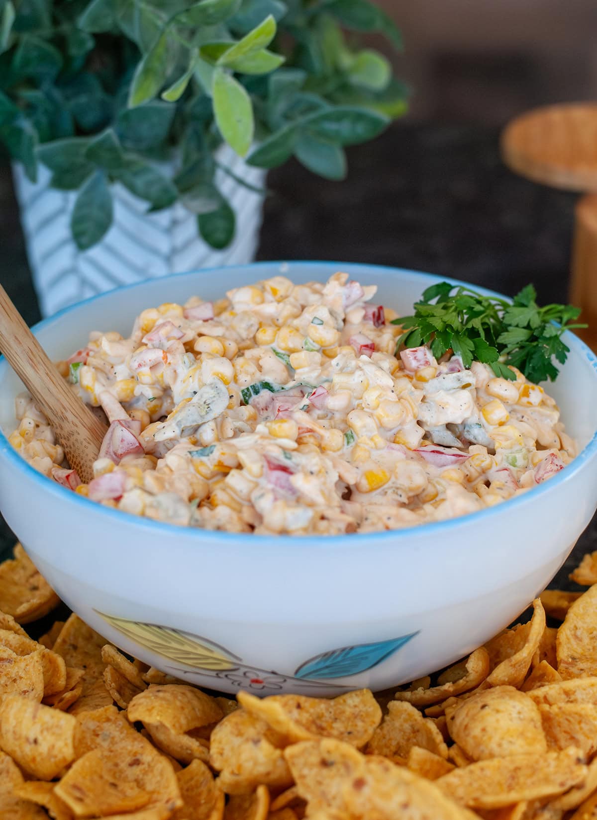 A bowl of corn dip surrounded by fritos.