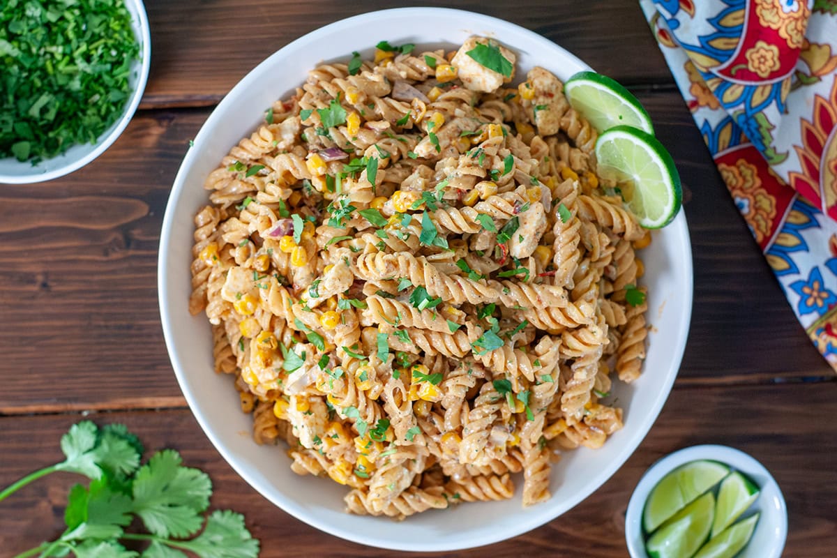 A top view of Mexican street corn pasta salad with lime wedges. 