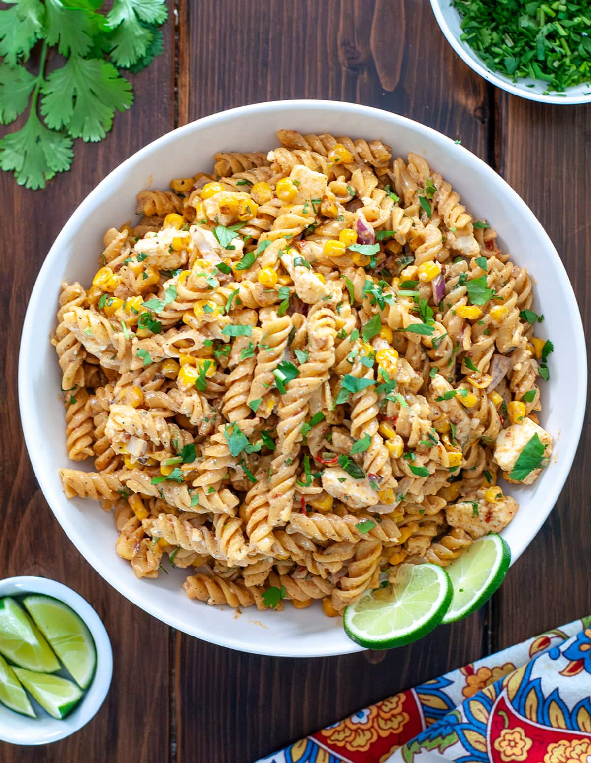 A bowl of Mexican street corn pasta salad showing corn, cheese crumbles, diced cilantro and fresh lime. 