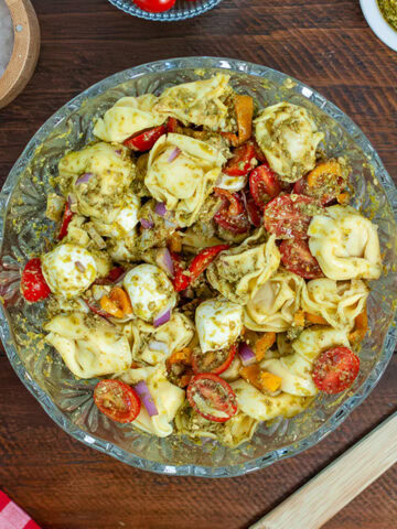 Pesto Tortellini Pasta in a glass bowl with tomatoes and mozzarella cheese.
