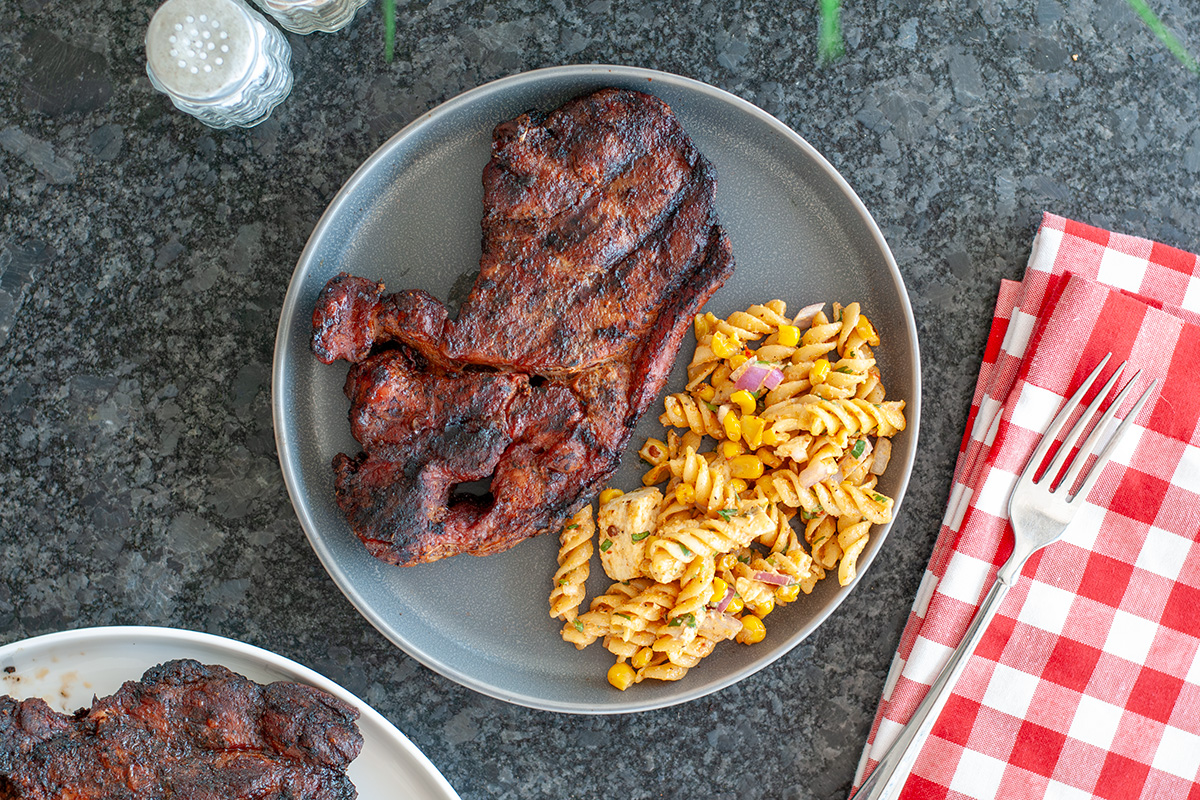 A top view of a pork steak served with pasta salad. 