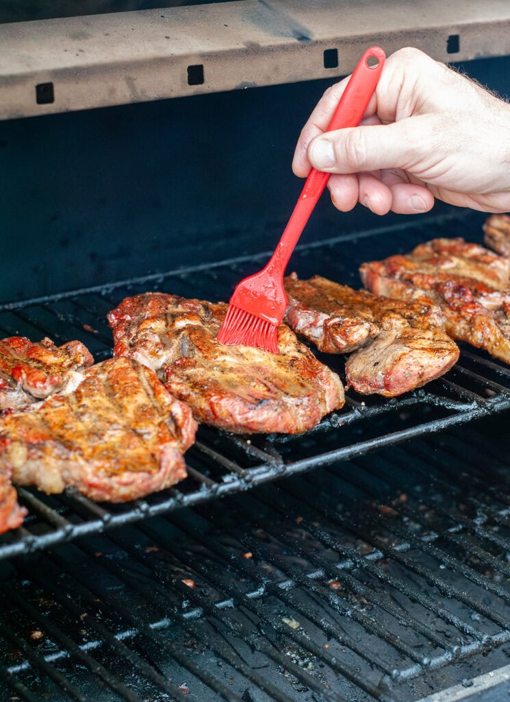 Pork steaks being basted on the top grill away from direct heat. 