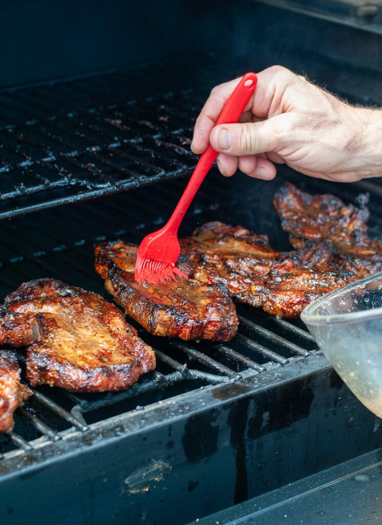 Finished pork steaks being basted on the grill. 