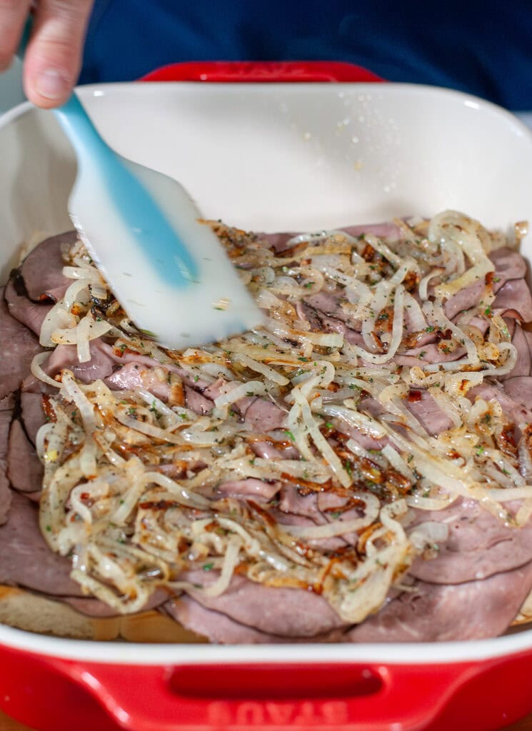 Sautéed onions being spread on the roast beef layer of the sandwiches. 