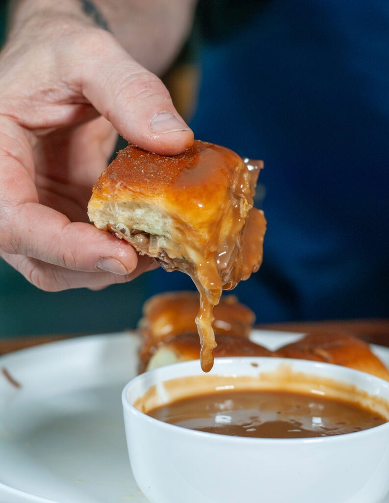 A sandwich being dipped in gravy. 