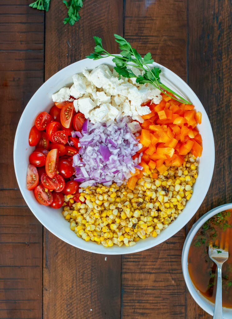 Tomatoes, feta, bell peppers, onion and roasted corn in a bowl.