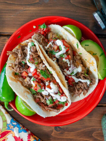Beef tacos on a plate by a slow cooker and limes.