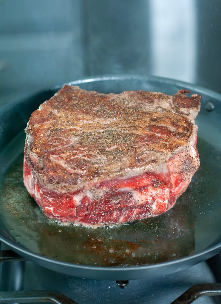The chuck roast in a skillet seasoned with salt and pepper. 