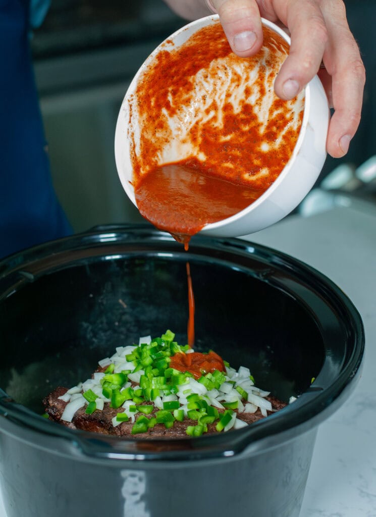 A photo of the sauce being poured over the chopped veggies and roast in crockpot. 
