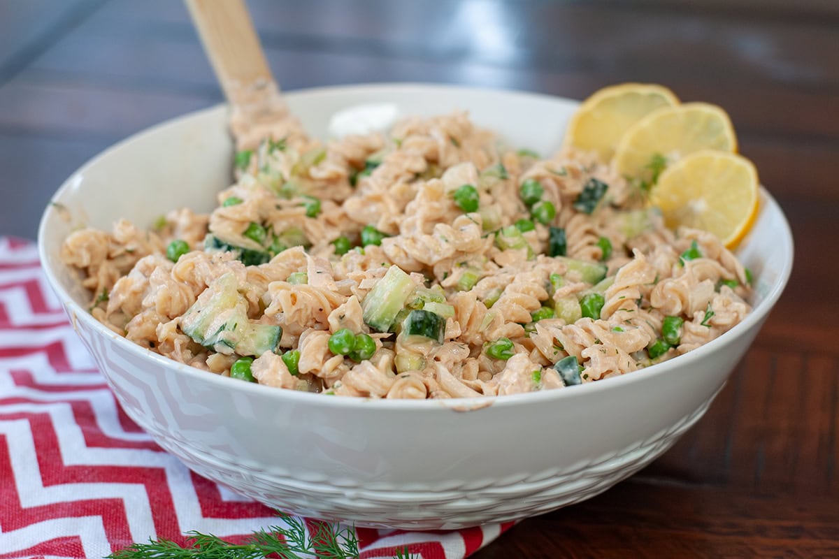 Tuna pasta salad in a bowl with slices of lemon and a wooden spoon.