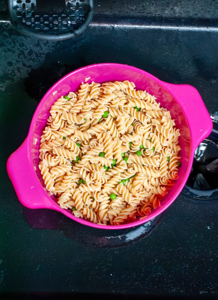 Noodles and frozen peas in a strainer.