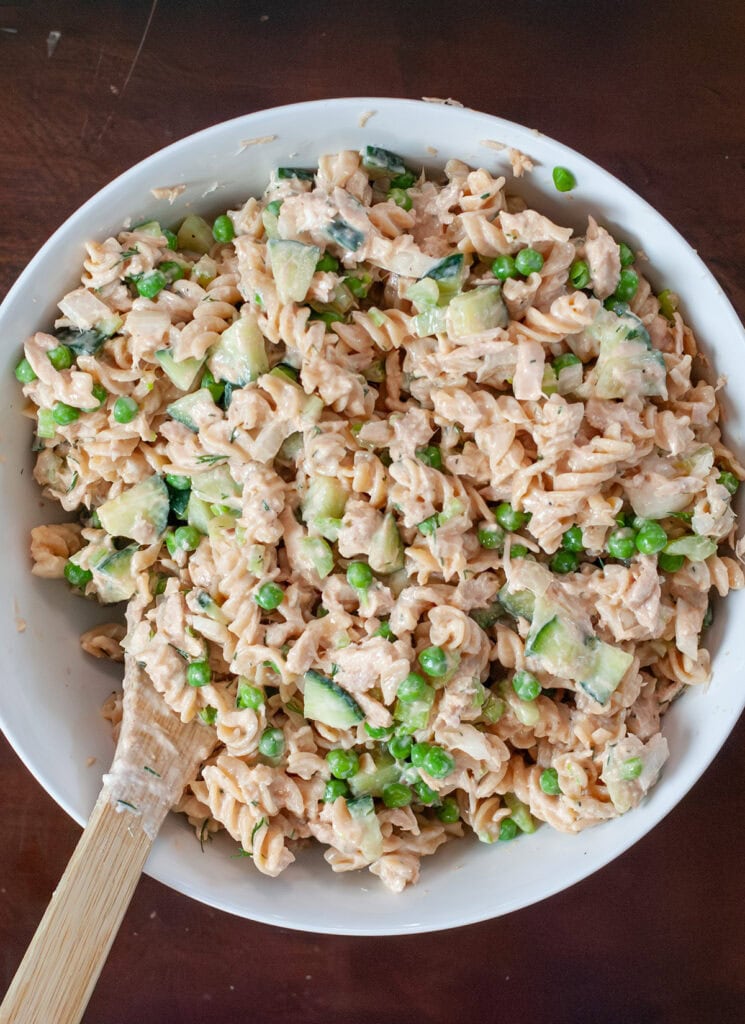 Tuna pasta salad ingredients being mixed with wooden spoon.