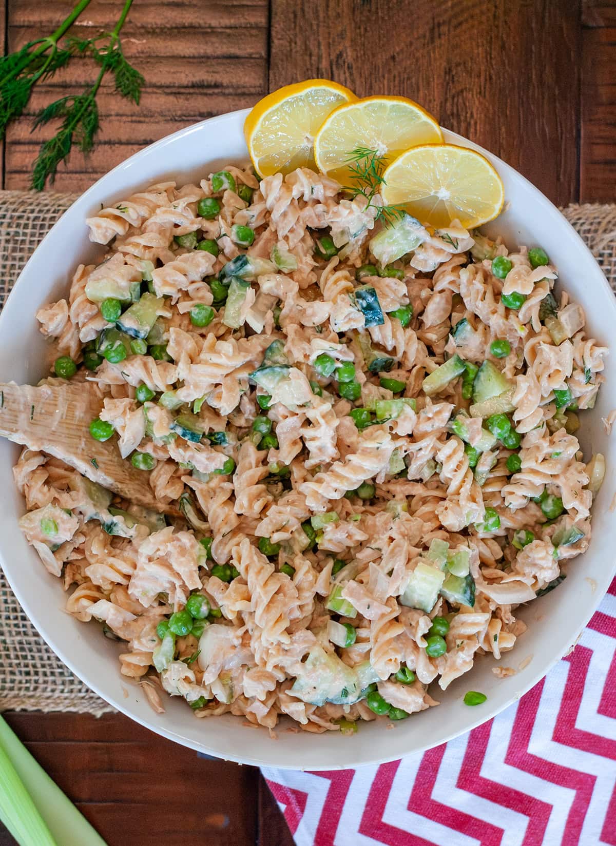 A top view of creamy tuna pasta salad with rotini pasta, peas cucumber, garnished with fresh dill and lemon slices. 