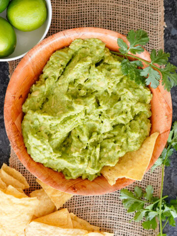 guacamole with limes and chips in a wooden bowl.