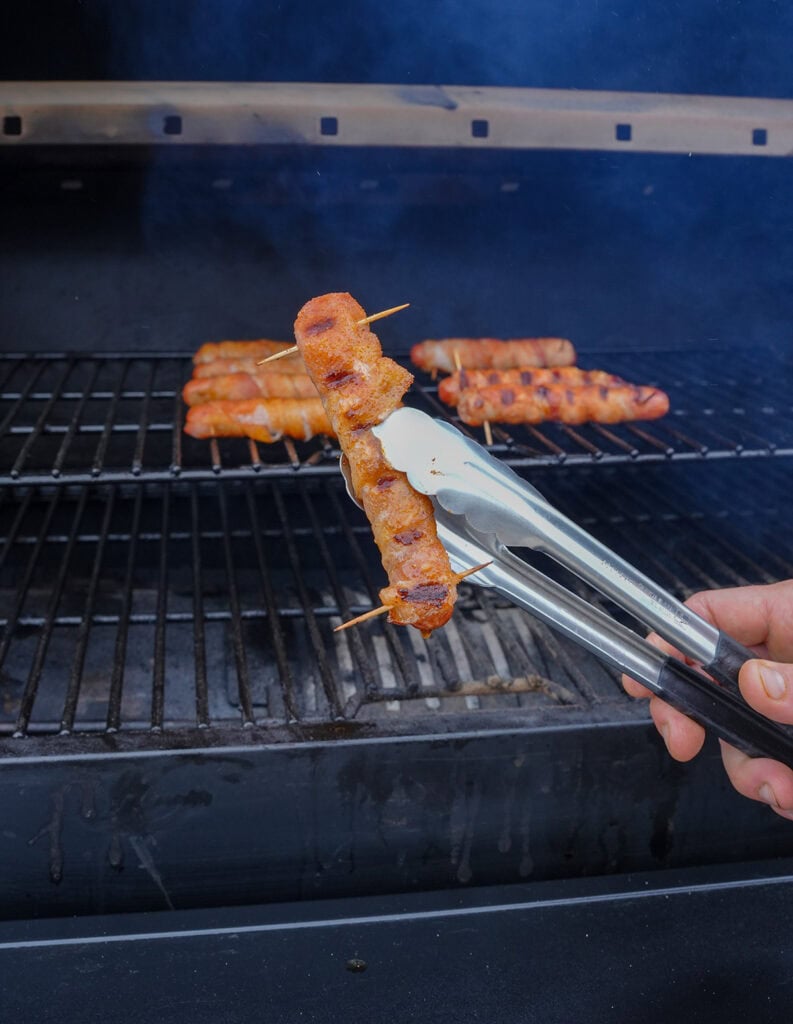 Tongs holding finished hot dog by the grill.