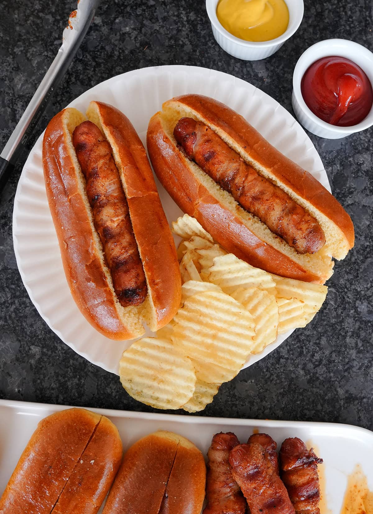 A top view of hot dogs on a paper plates served alongside chips.