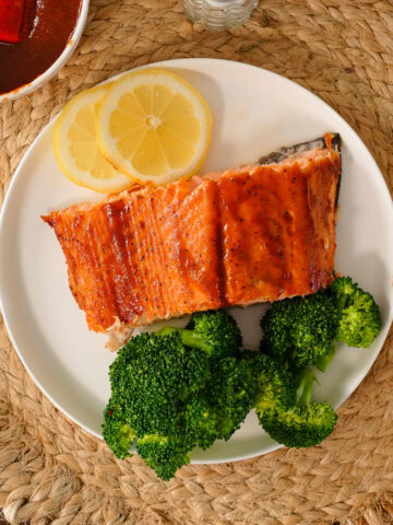 A slice of salmon with barbecue sauce next to broccoli and lemon.