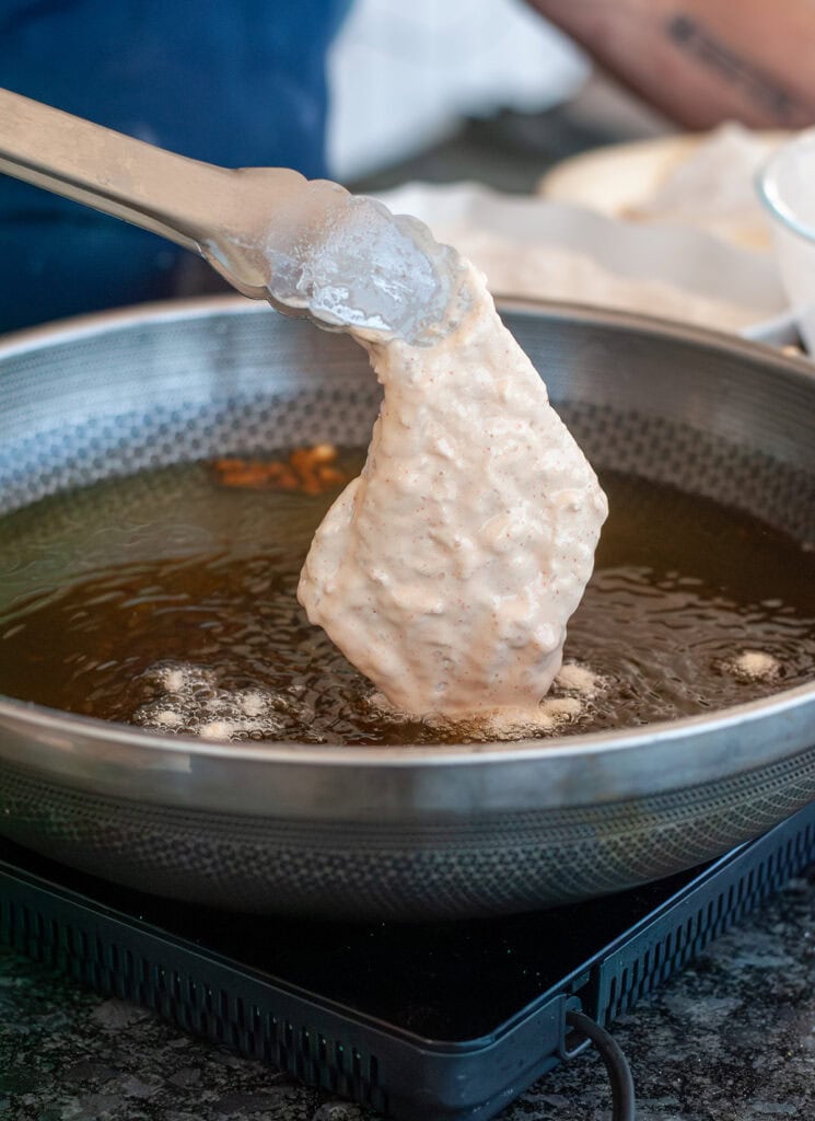 Fish going into hot oil in frying pan.