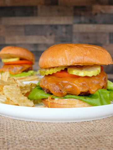 2 Butter Burgers on plates with potato chips.