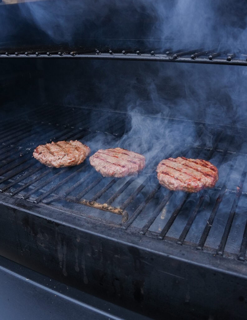 Three butter burgers on the grill cooking with grill marks. 