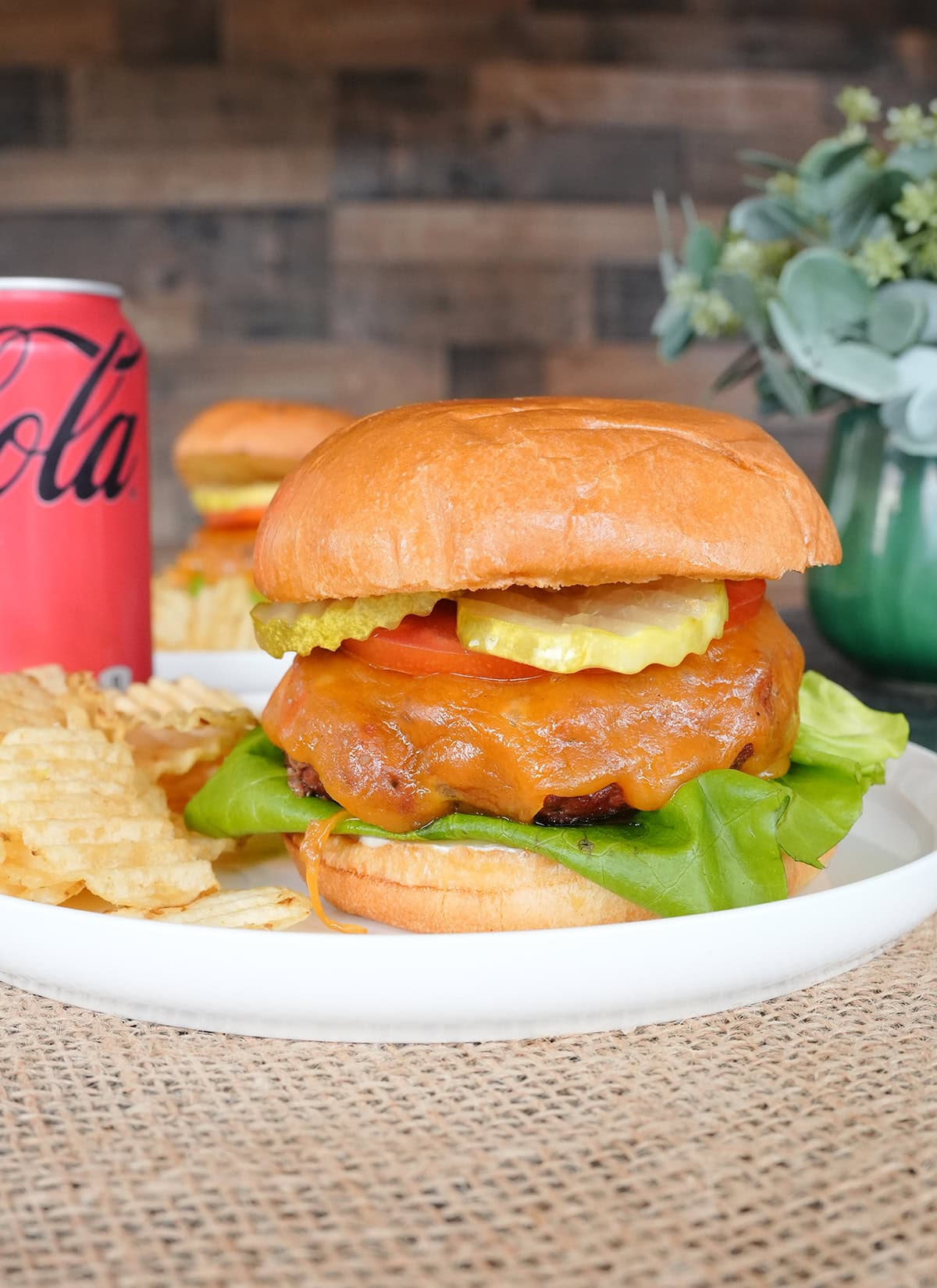 A butter burger with pickles, lettuce and tomatoes served with chips. 