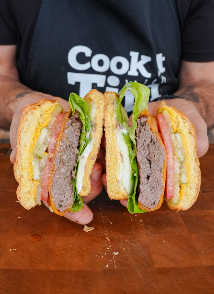 A finished butter burger cut in half showing the burger, lettuce, tomato, pickles and cheese.