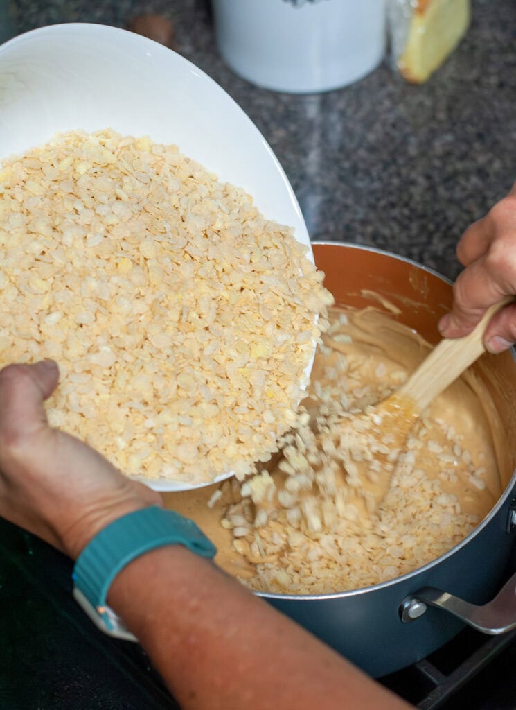 Rice Krispie cereal being added into the melted mixture in a pot. 