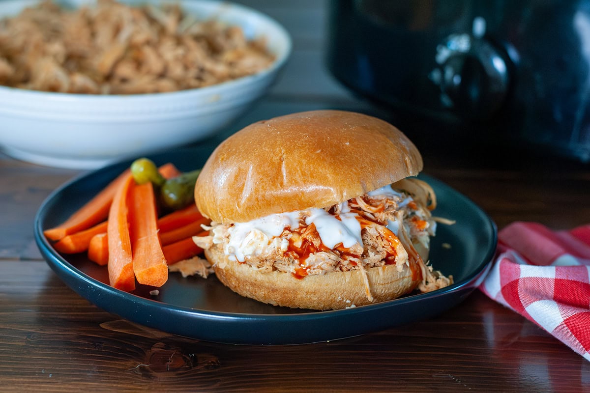 A shredded chicken sandwich sitting on a plate with carrots. 
