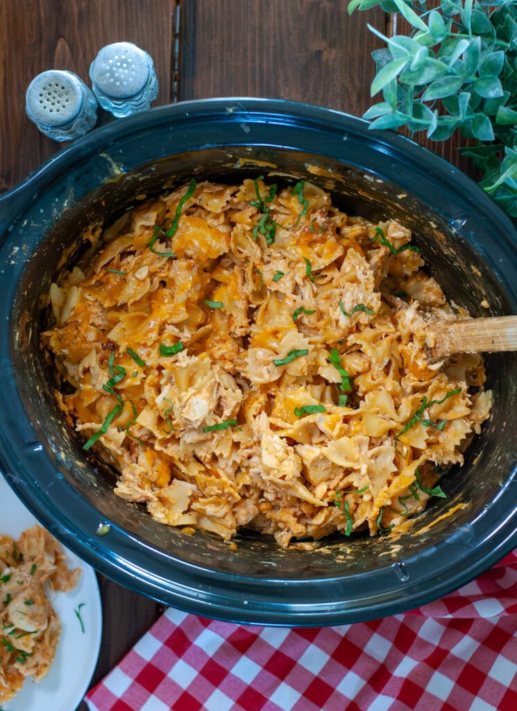 A top view of mac and cheese showing pasta, chicken, and fresh parsley in the crock pot. 